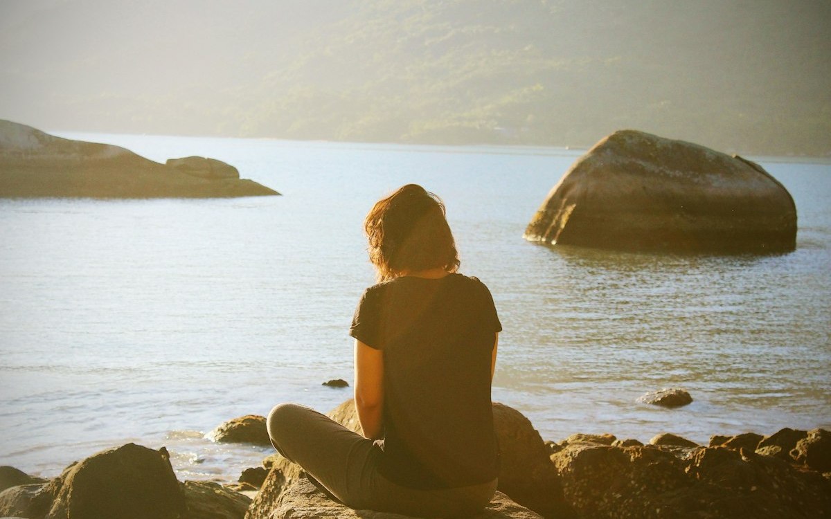 Person seated in meditation by the water, viewed from behind